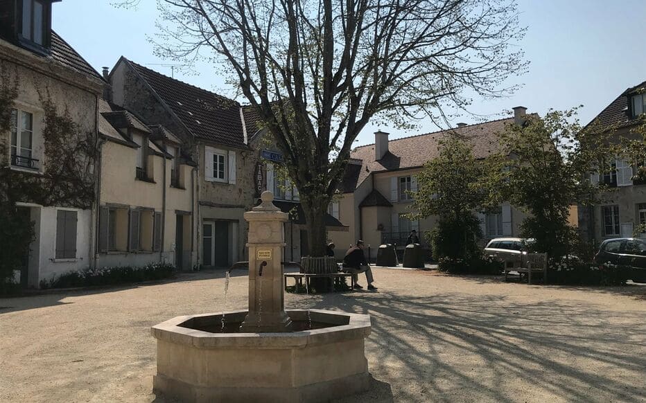 Photo d'une petite fontaine au premier plan avec des maison ancienne en arrière plan.